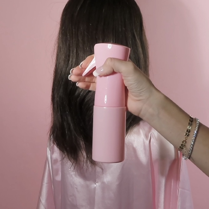 holding pink spray bottle in front of mannequin head with extensions