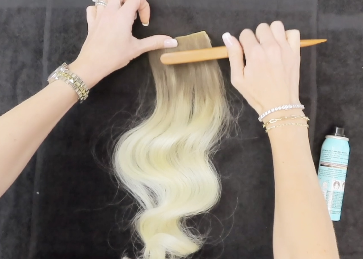 brushing root spray product into hair extensions 