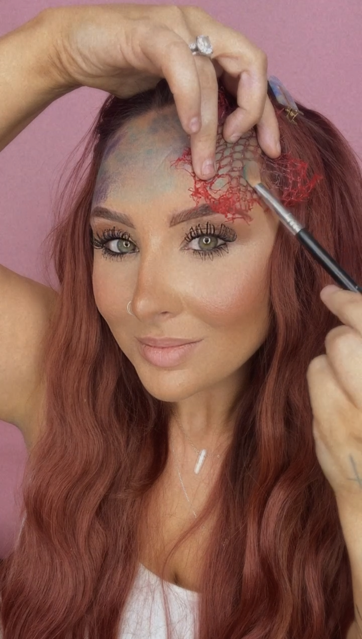 girl applying blue eyeshadow on top of a fishnet to make scales