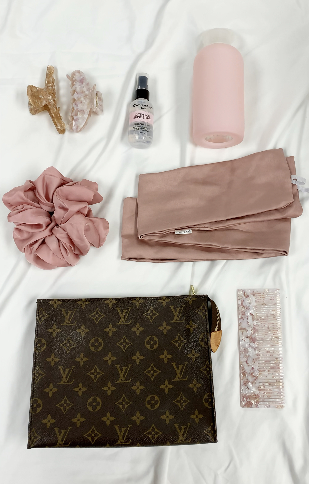 silk scrunchie, water bottle, shine spray, clips, comb, silk scarf and bag on bed sheet bedside essentials