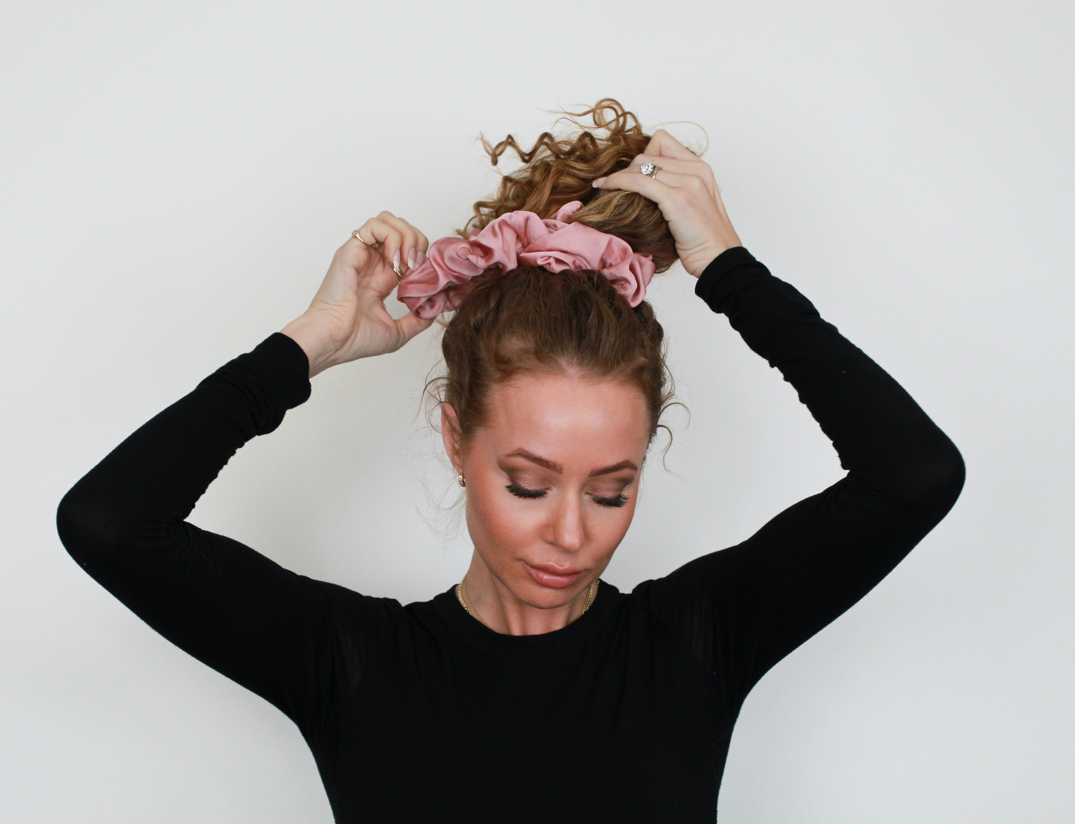 woman putting curly hair up in aa loose ponytail with large silk scrunchie