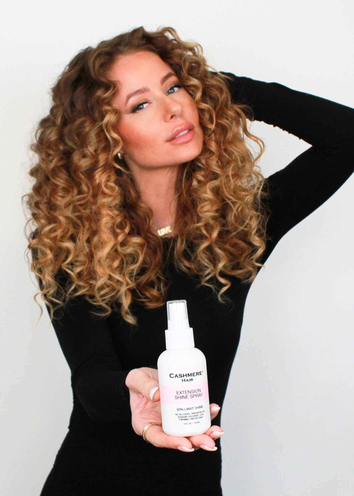 woman with curly hair wearing clip-in extensions holding the cashmere hair extension shine spray